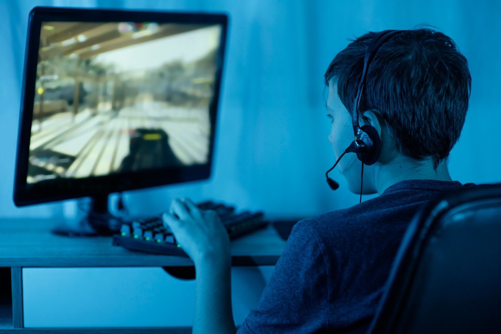 a young boy wearing a headset and playing a video game on a computer